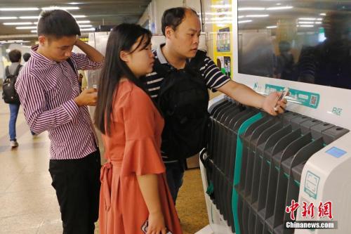 圖為沒(méi)帶雨傘的民眾在共享雨傘的貨架上掃碼借用。殷立勤 攝