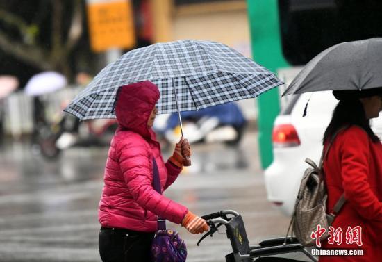 資料圖：昆明市區(qū)里身著羽絨服冒雨趕路的民眾。 中新社記者 李進紅 攝